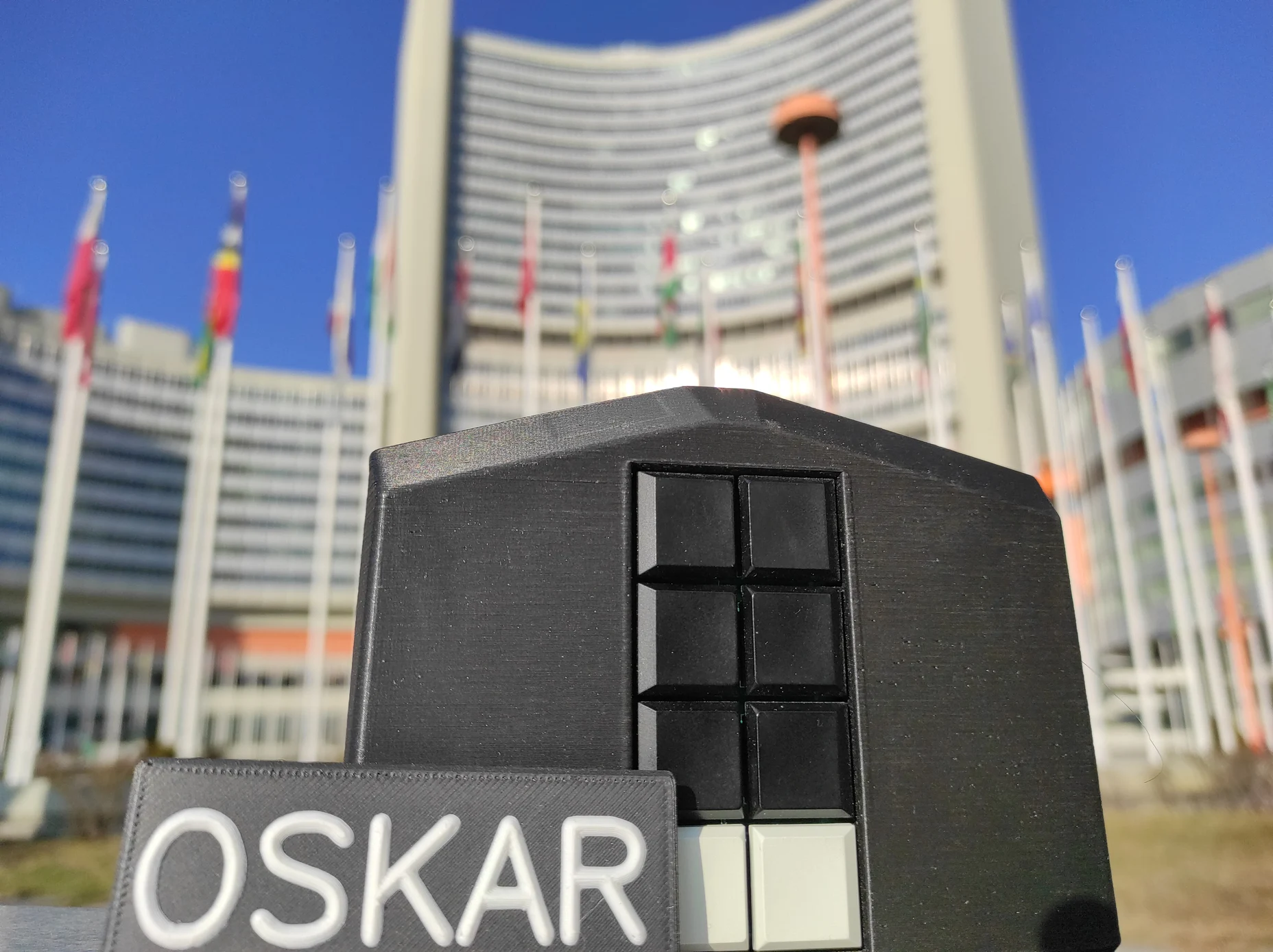 Eine mobile Brailletastatur mit 8 Tasten in den Farben schwarz und weiß vor den UNO-Gebäuden in Wien.  Davor steht ein Schild mit der Beschriftung Oskar in Großbuchstaben.